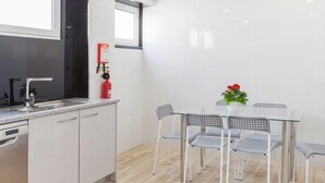 Eine moderne Küche mit weißen Schränken, einer Spüle aus Edelstahl und einem Fenster über der Arbeitsplatte. Eine Feuerlöscher ist an der Wand angebracht.