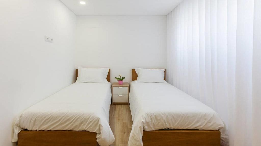 Habitación doble con dos camas individuales, una mesita de noche con una planta y una pared blanca.