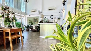 Una habitación amplia con suelo de madera, una mesa de comedor de madera y sillas. Hay plantas en macetas y un ventanal grande que proporciona luz natural.