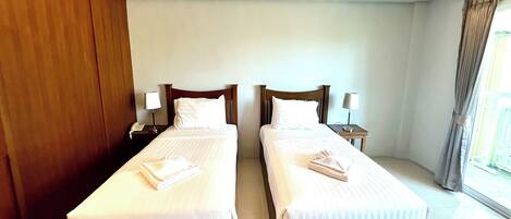 A hotel room with two single beds, each with a pillow and a folded towel. There are bedside tables with lamps and a telephone.