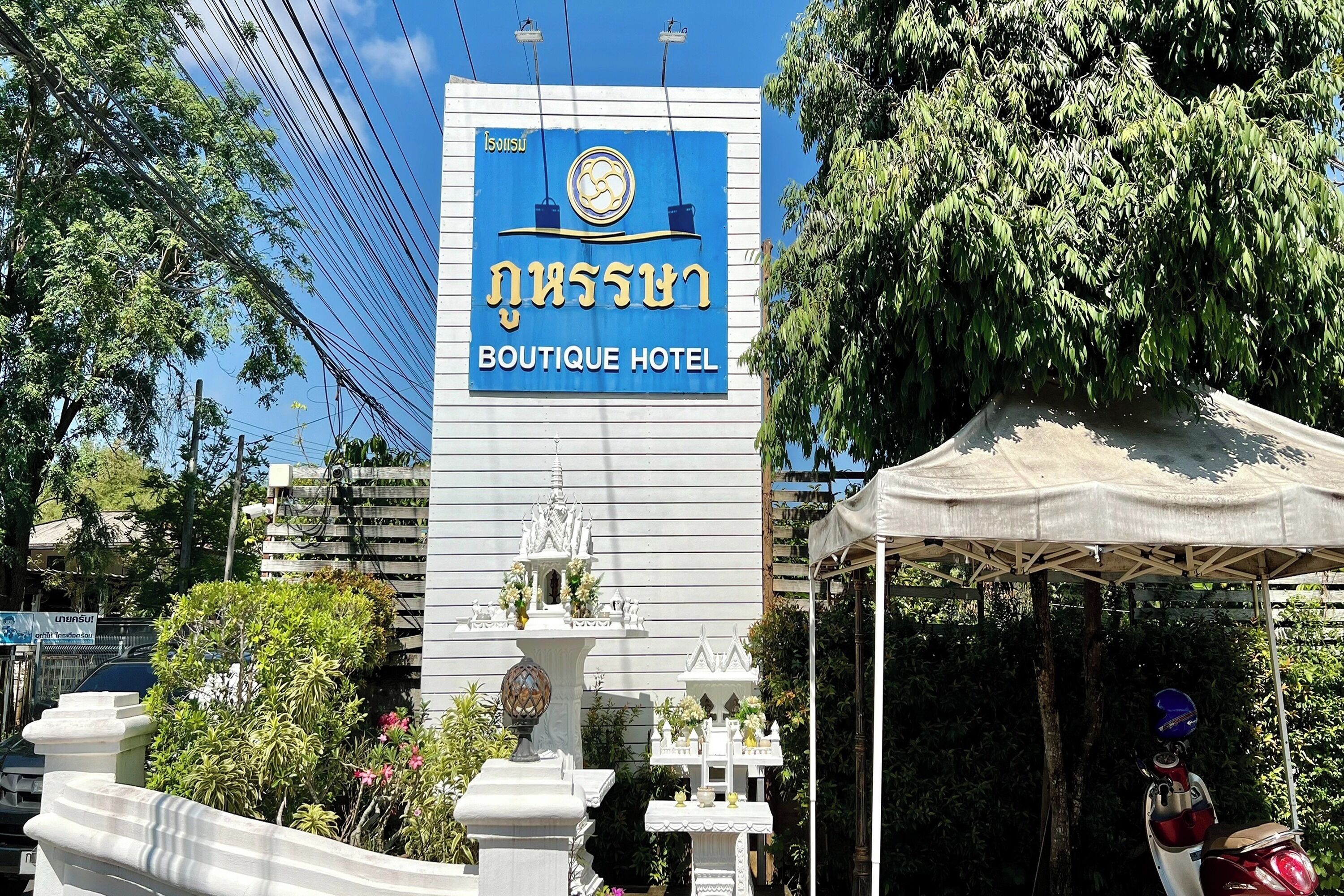 Letrero del Boutique Hotel, con diseño tailandés tradicional, un edificio blanco y una pequeña estructura similar a un santuario en el frente.