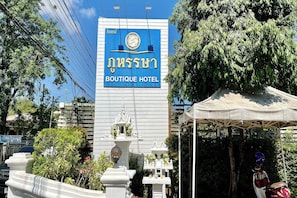 A sign for Boutique Hotel with a traditional Thai design, a white building, and a small shrine-like structure in front. - Phu Hun Sa Boutique Hotel (Nan)