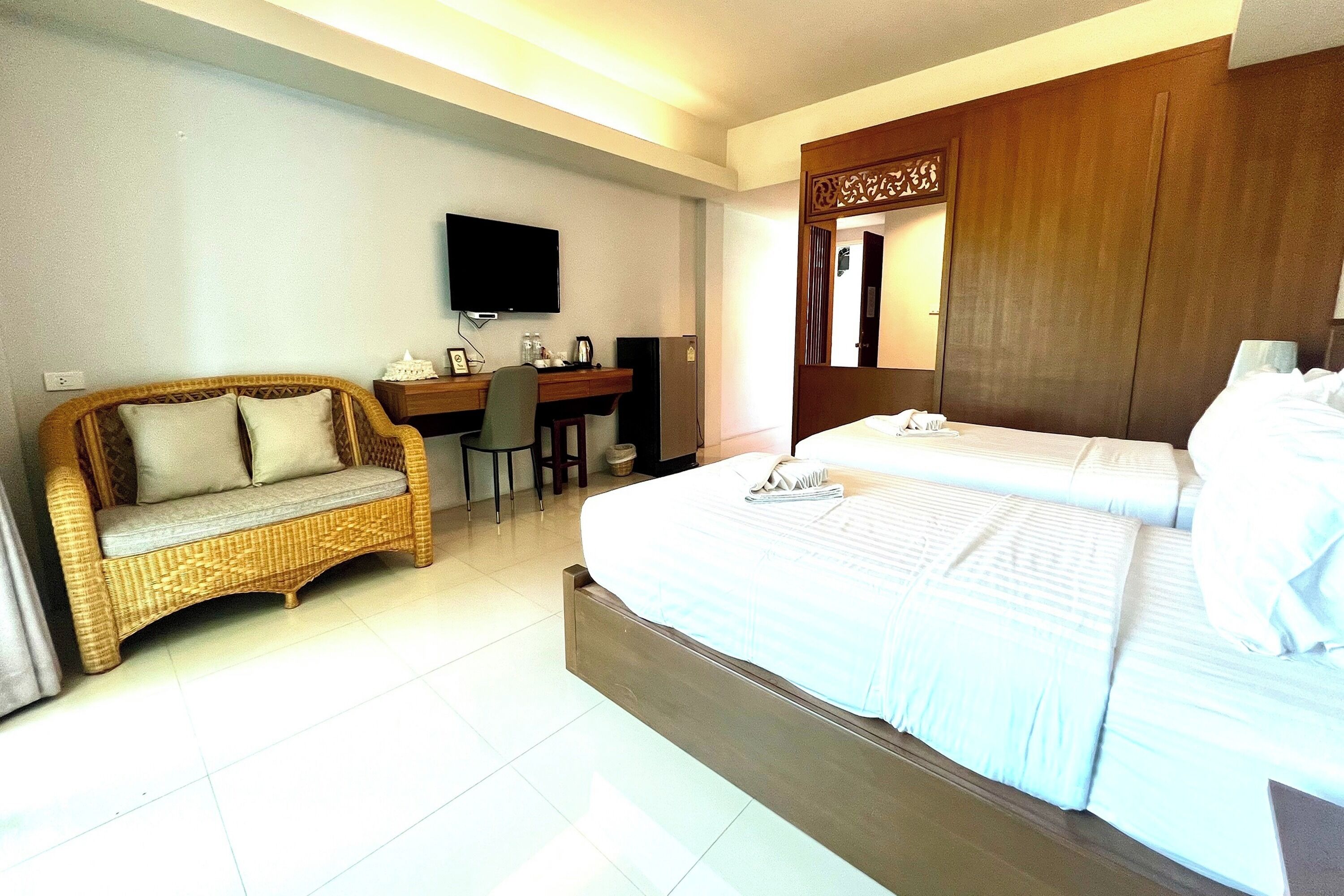 A hotel room with a bed, a desk with a chair, a television, and a wicker sofa.