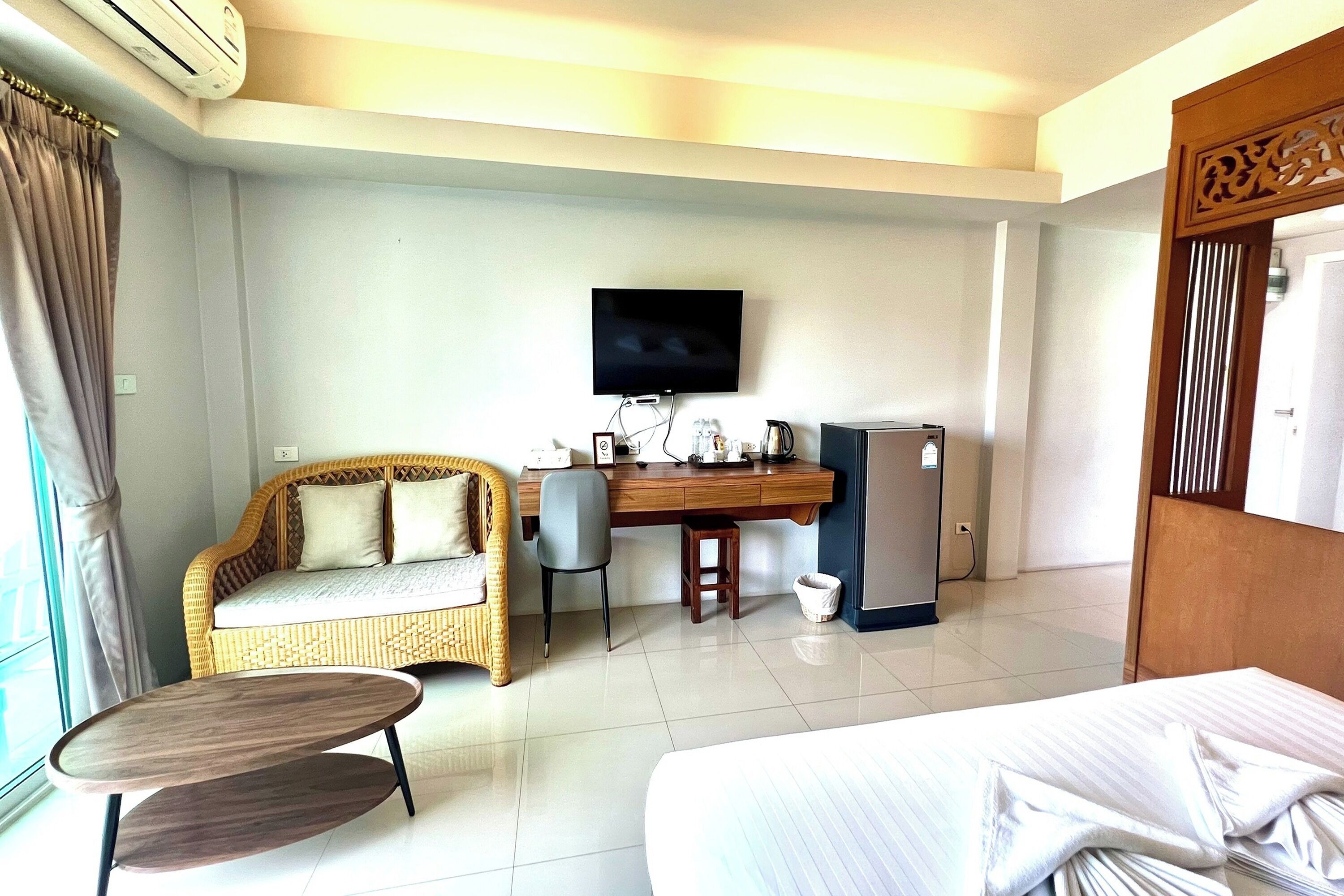 A hotel room with a bed, a desk with a computer, a chair, a sofa, and a television.