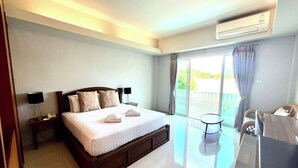 Habitación de hotel con una cama grande, una mesita, una silla y un balcón con cortinas.