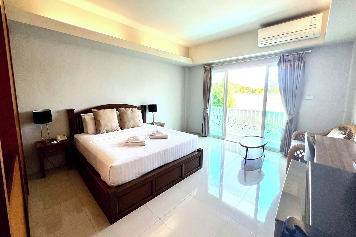 A hotel room with a large bed, a small table, a chair, and a balcony with curtains.