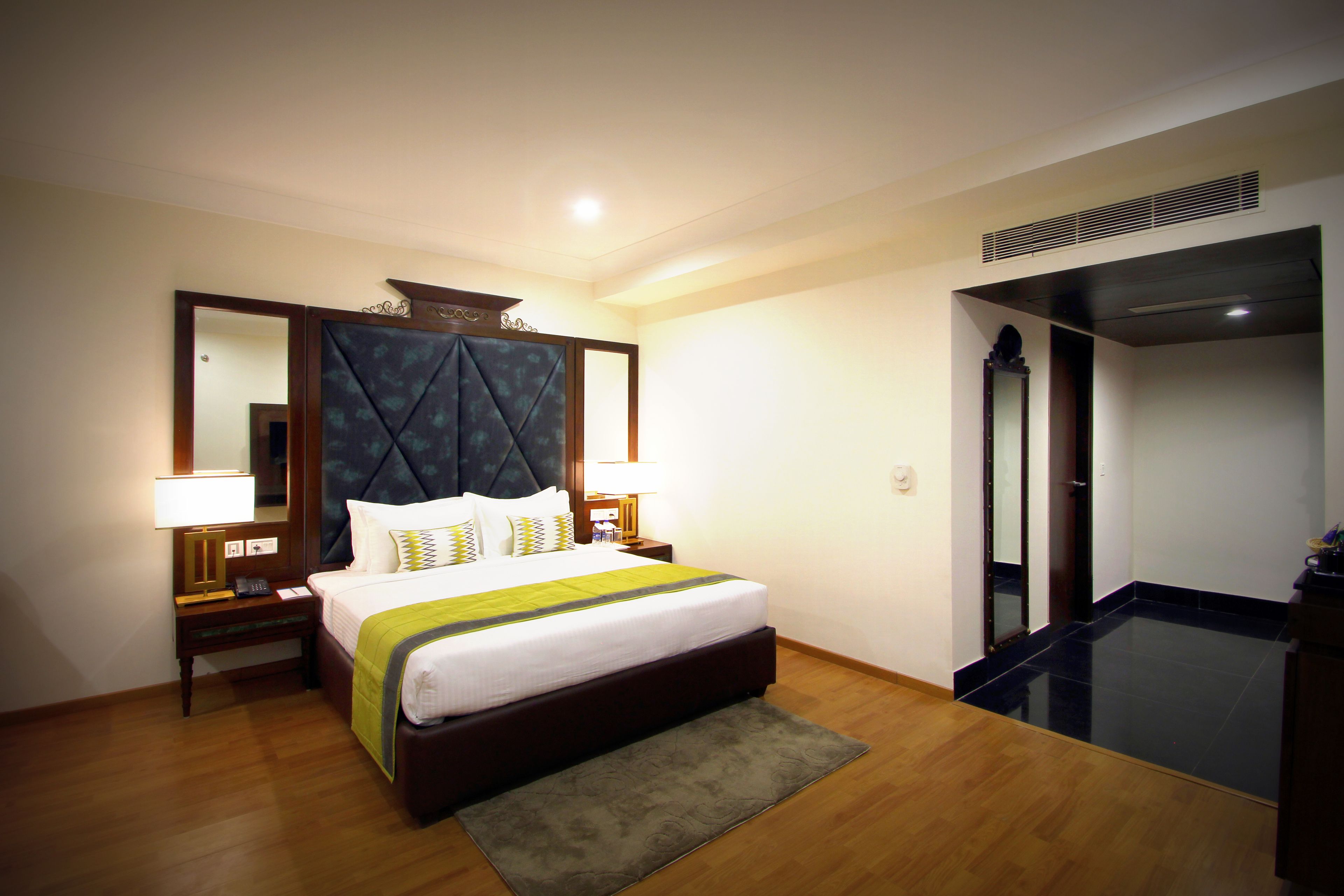 A hotel room with a large bed, two bedside tables with lamps, a mirror, and a small bathroom area.