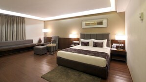 A hotel room with a large bed, a sofa, a small table, and two nightstands with lamps.