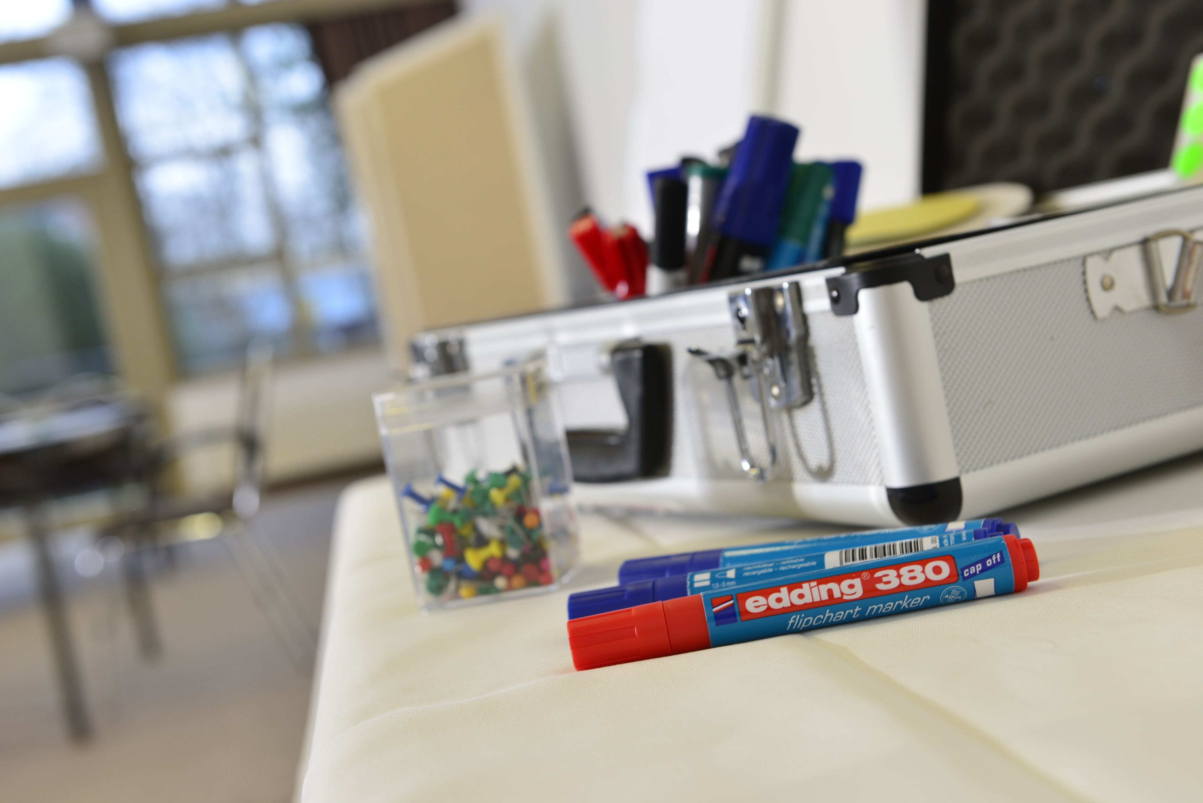 A desk with a laptop, a pen holder with pens, and a small container of colorful items.