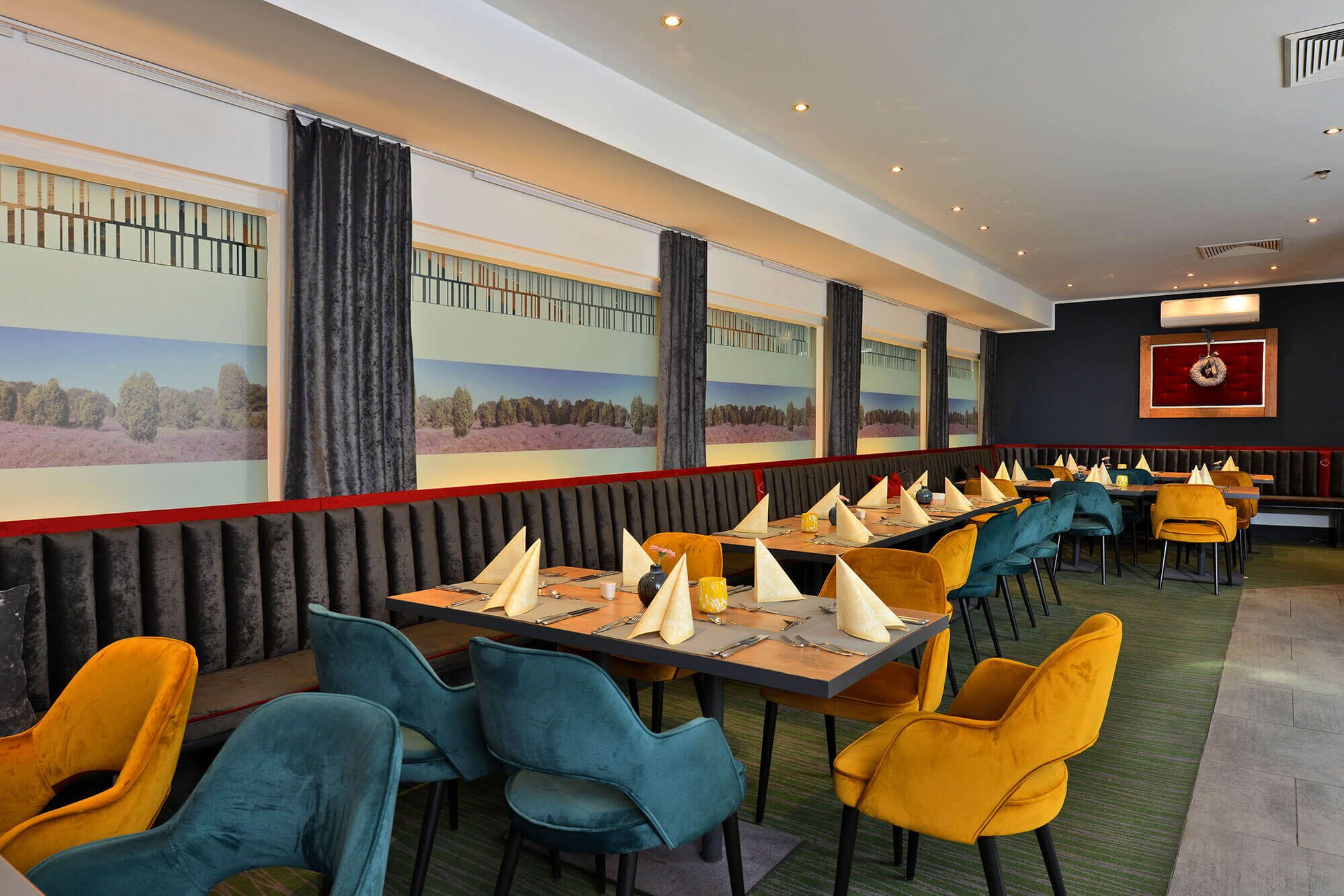 Un restaurant avec de longues tables, des chaises et une grande fresque murale.