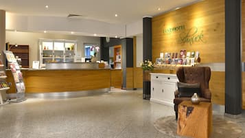 A reception area with a wooden reception desk, a brown armchair, and a small wooden table with a vase.