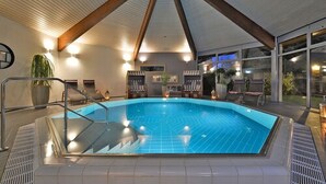 Una piscina interior con suelo de baldosas, borde de cristal y estructura de techo de madera.