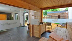 Interior de madera con sauna, terraza de madera y vista a una cabaña de madera en el exterior.
