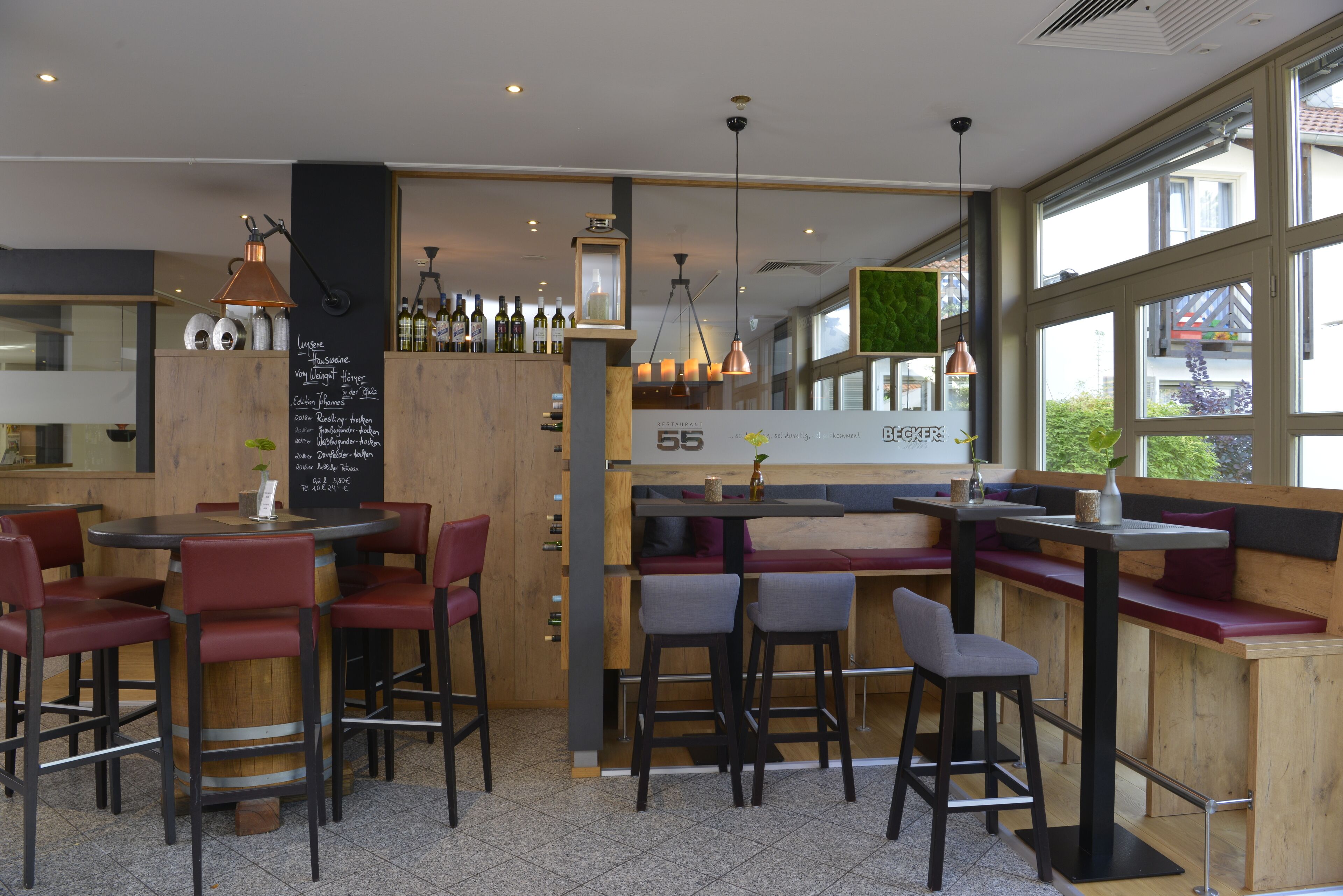 Un restaurante con mesas y sillas de madera, una zona de bar y amplios ventanales.