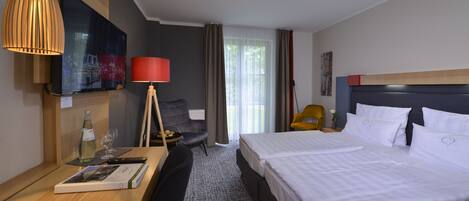 Habitación de hotel con cama, escritorio con lámpara, silla, televisor y ventana con cortinas.