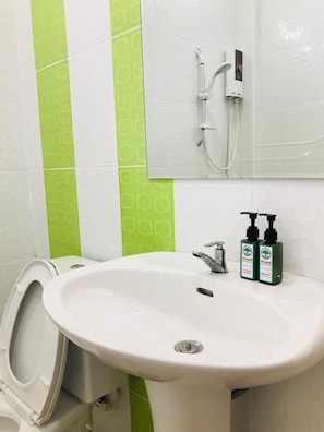 Un baño con un lavabo blanco, un inodoro y una ducha. Hay dos botellas de champú en el lavabo.