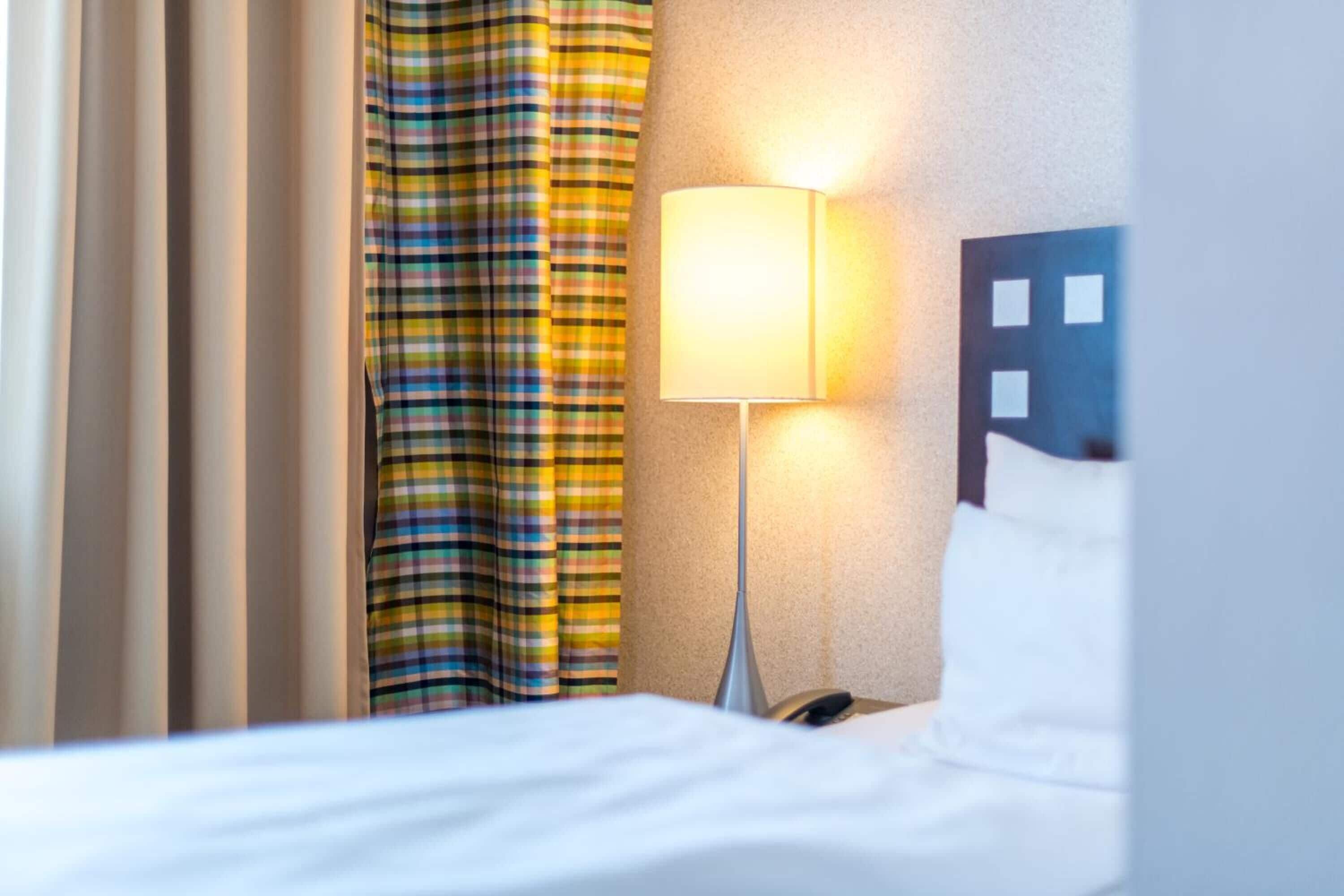 A hotel room with a bed, a nightstand with a lamp, and a window with curtains.