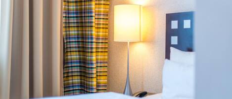 A hotel room with a bed, a nightstand with a lamp, and a window with curtains.