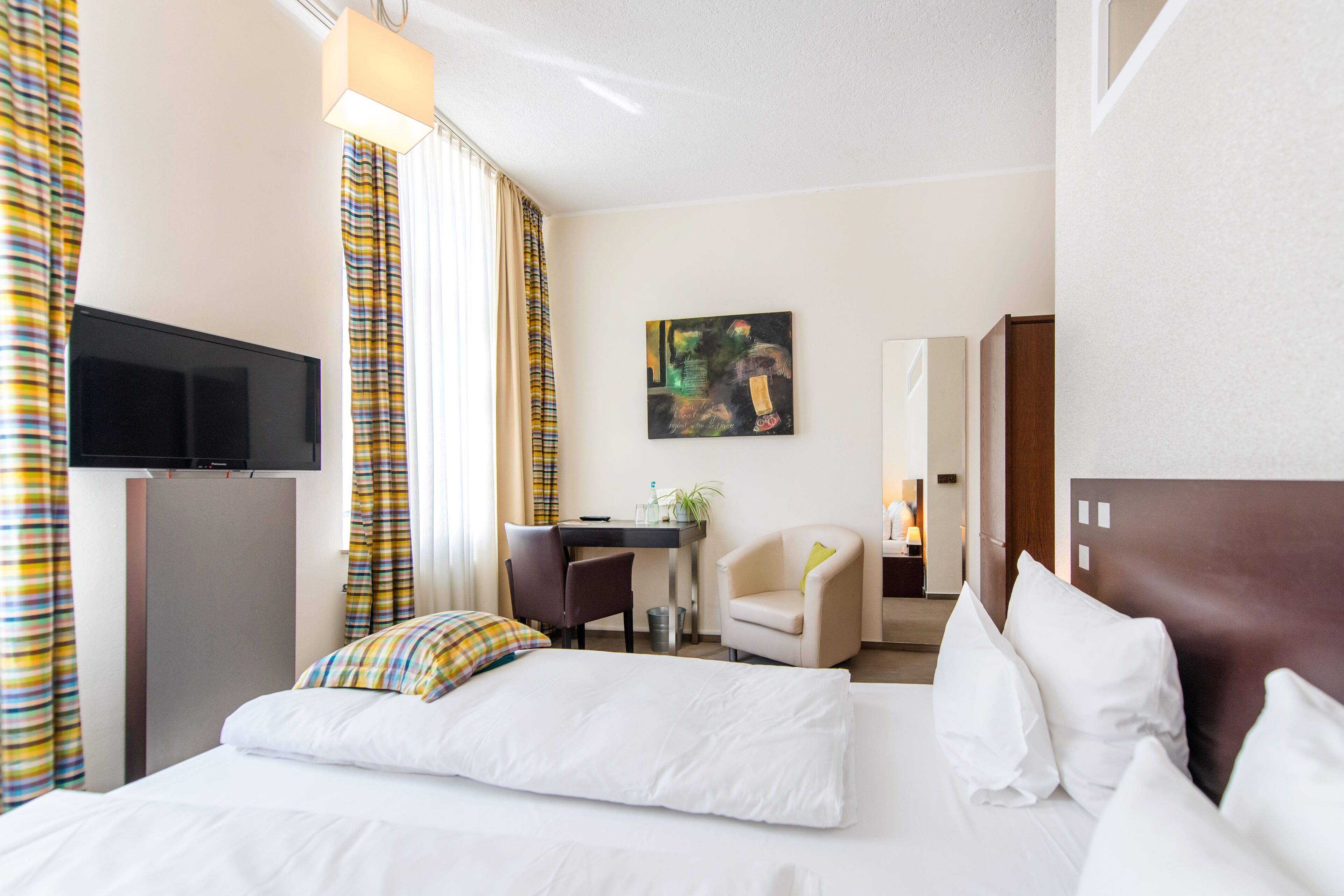 Una habitación de hotel con una cama, un escritorio, una silla, un televisor y un cuadro en la pared.