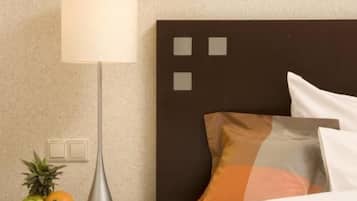 Une chambre d’hôtel bien rangée, avec un lit, une table de chevet dotée d’une lampe et un panier de fruits.