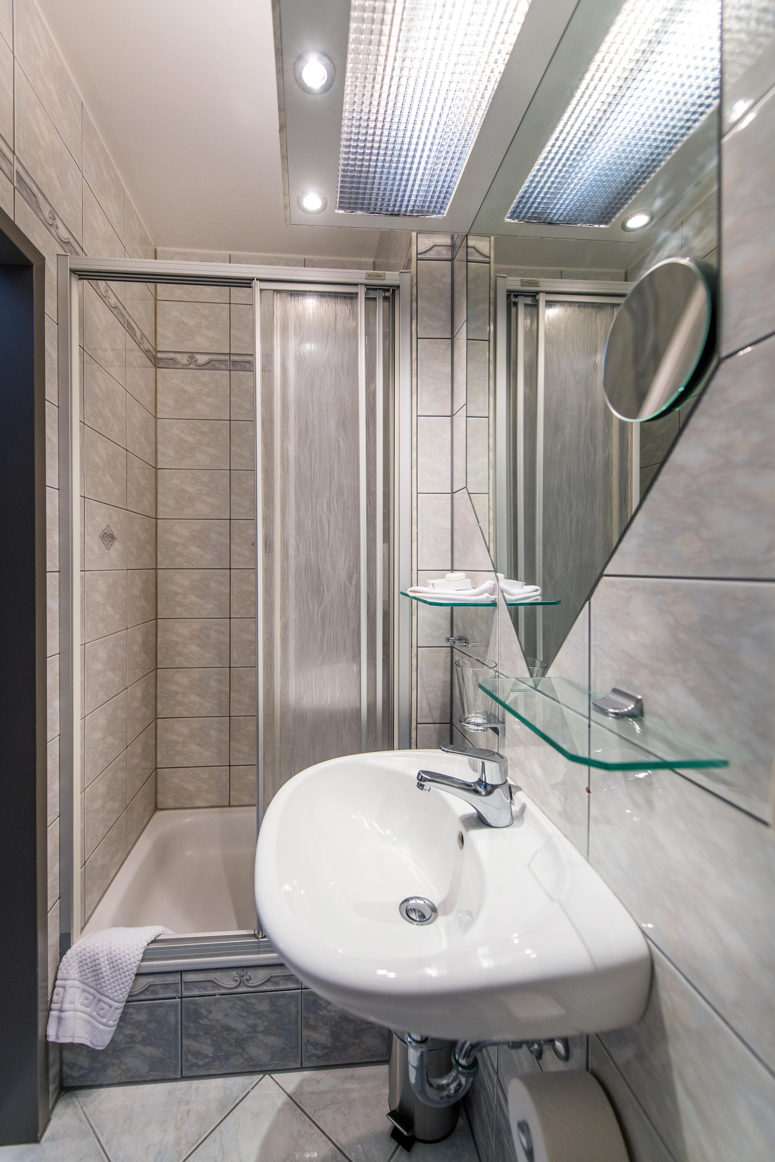 Un baño moderno con cabina de ducha de vidrio, un lavamanos blanco y un espejo.
