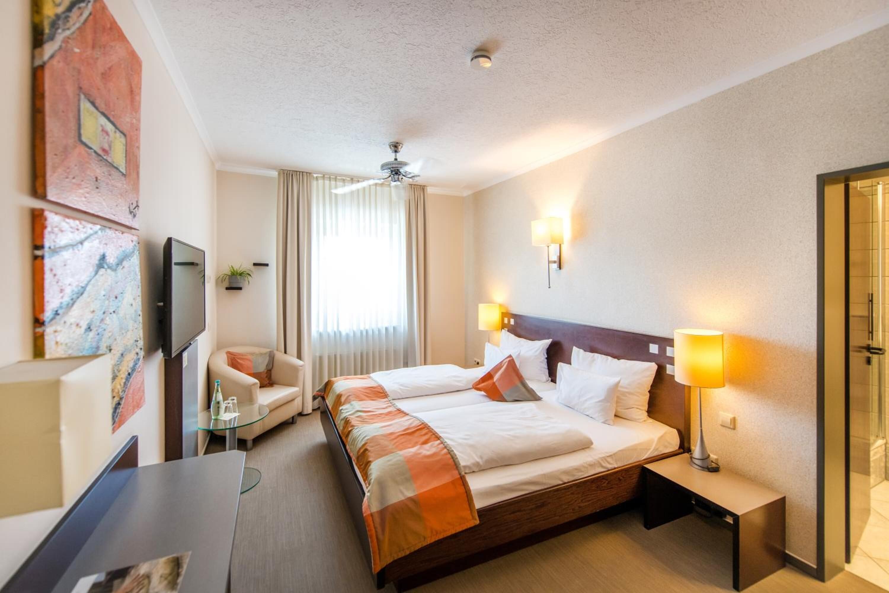 Una habitación de hotel con una cama grande, un escritorio, una silla, un televisor y un ventilador de techo.