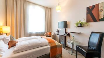 Une chambre d’hôtel comprenant un lit, un bureau avec un ordinateur, une chaise, une petite table, une plante et un téléviseur.