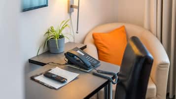 Habitación de hotel con escritorio, teléfono, control remoto, planta y cojín.