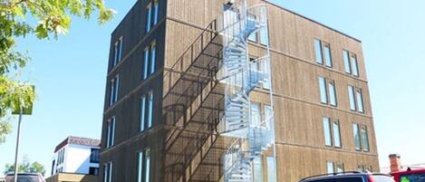 A multi-story building with a spiral staircase on the side, parked cars, and a clear sky.