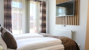 Habitación de hotel con una cama, un televisor montado en la pared y un ventanal con cortinas.