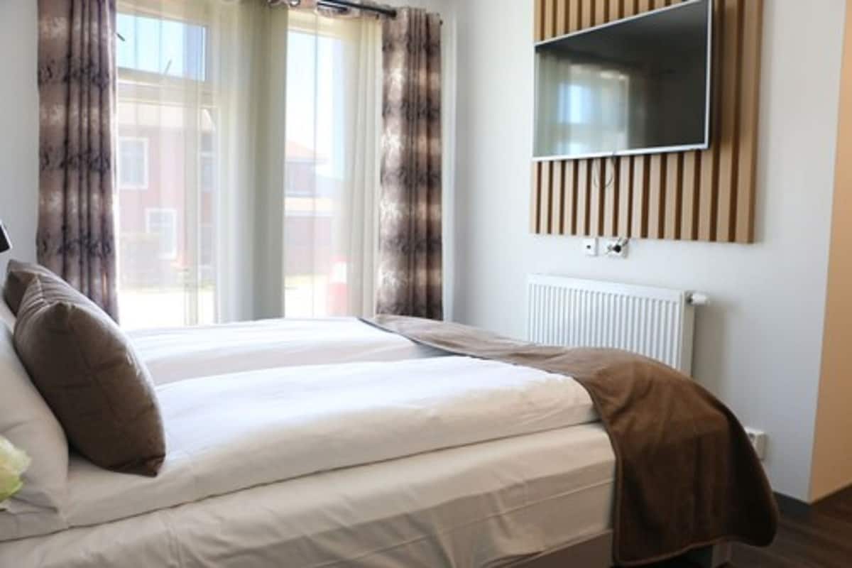 A hotel room with a bed, a TV mounted on the wall, and a window with curtains.