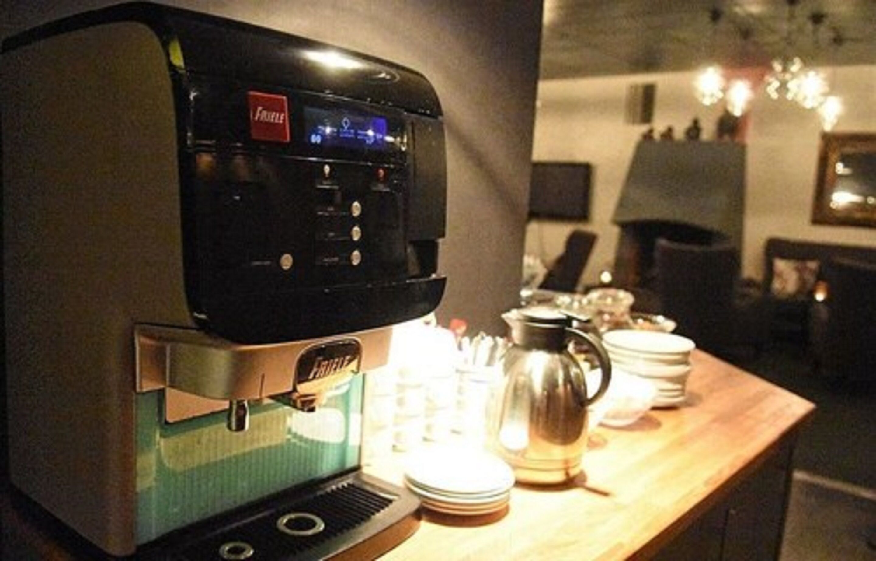 A coffee machine with a digital display, a kettle, and stacked plates on a wooden table in a room with a modern design.