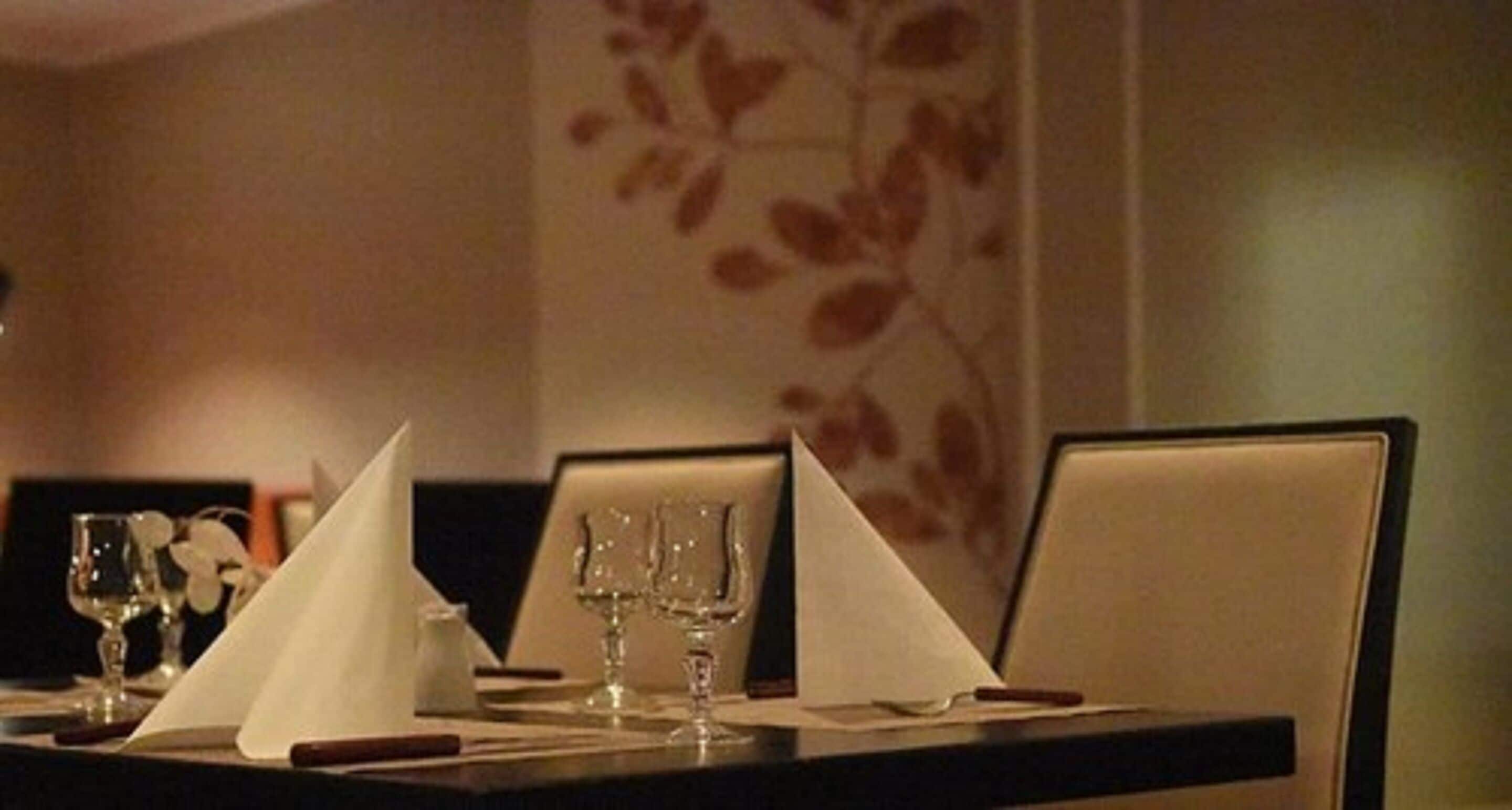 Une table à manger dressée avec une serviette blanche, deux verres à vin et un petit vase.