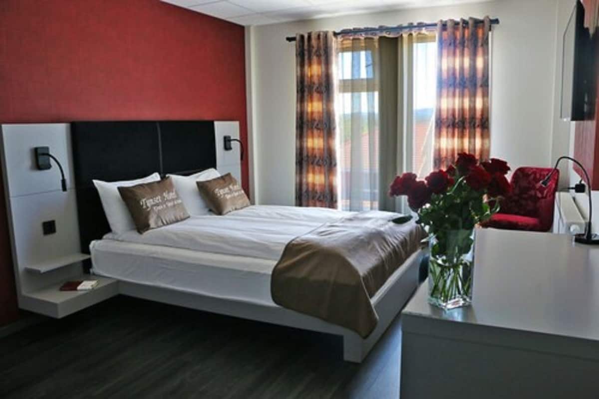 A modern hotel room with a bed, bedside tables, a desk, and a vase of flowers.