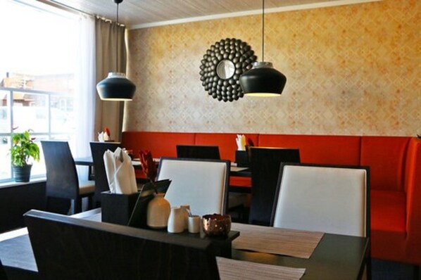 A restaurant with a red cushioned bench, black chairs, and a patterned wall.