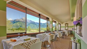 A restaurant with tables set for dining, large windows offering mountain views, and a green and white color scheme. - Hotel Europa (Sorico)