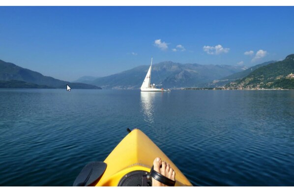 A kayak on calm water with a sailboat in the distance and mountains in the background. - Hotel Europa (Sorico)
