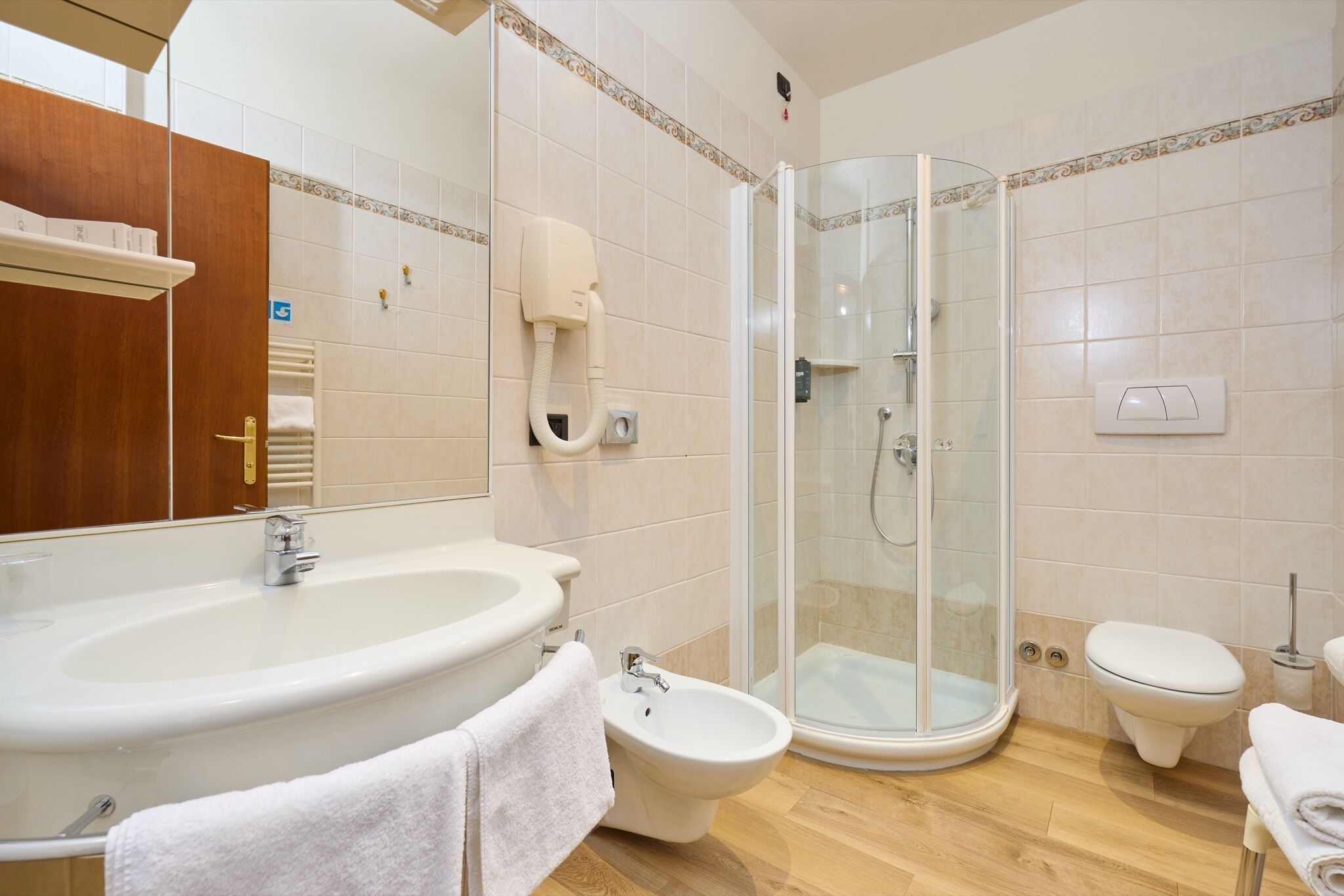 Un baño con lavamanos grande, bidé, inodoro y ducha con mampara de cristal.