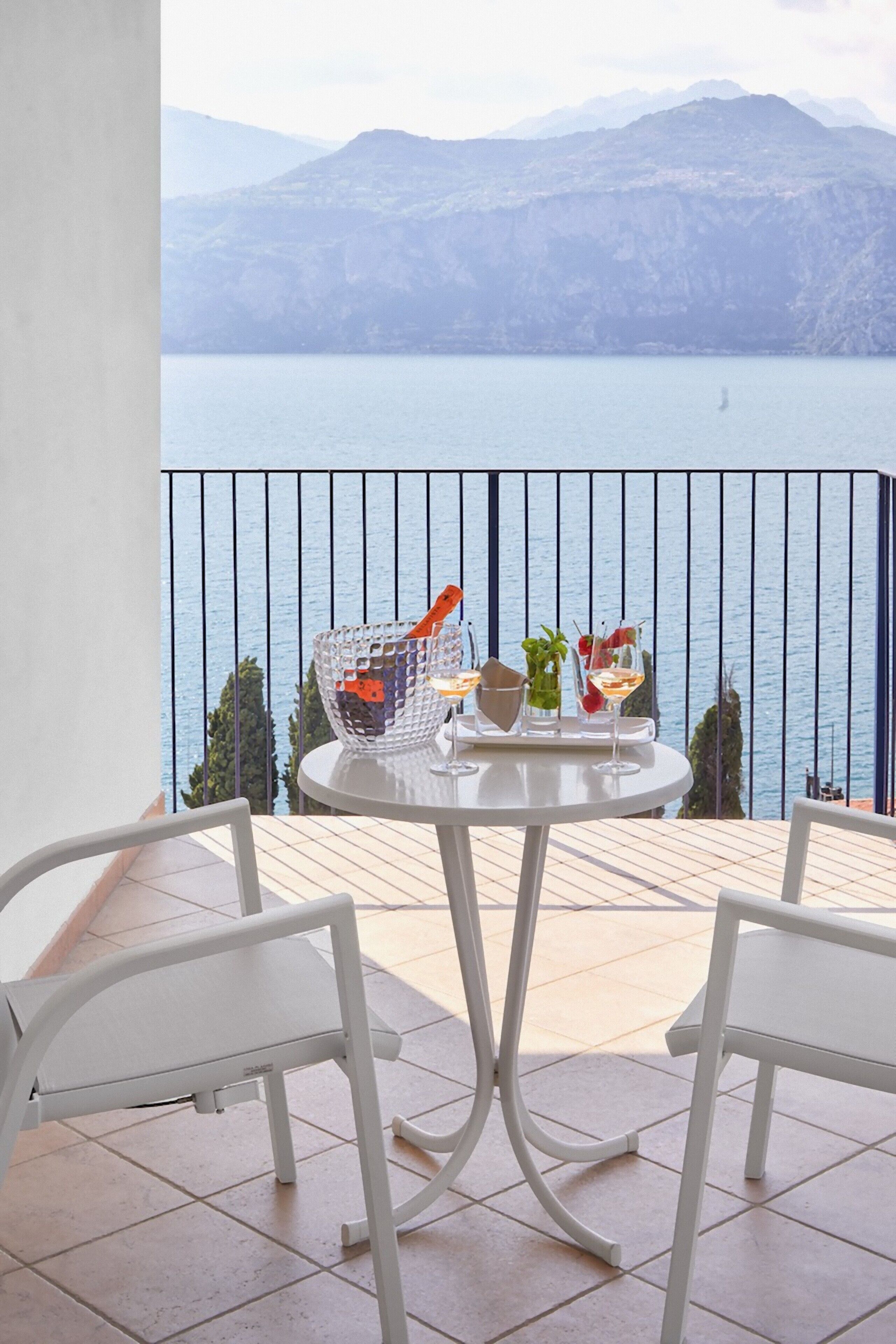 A balcony with a table set for two, overlooking a body of water and mountains.