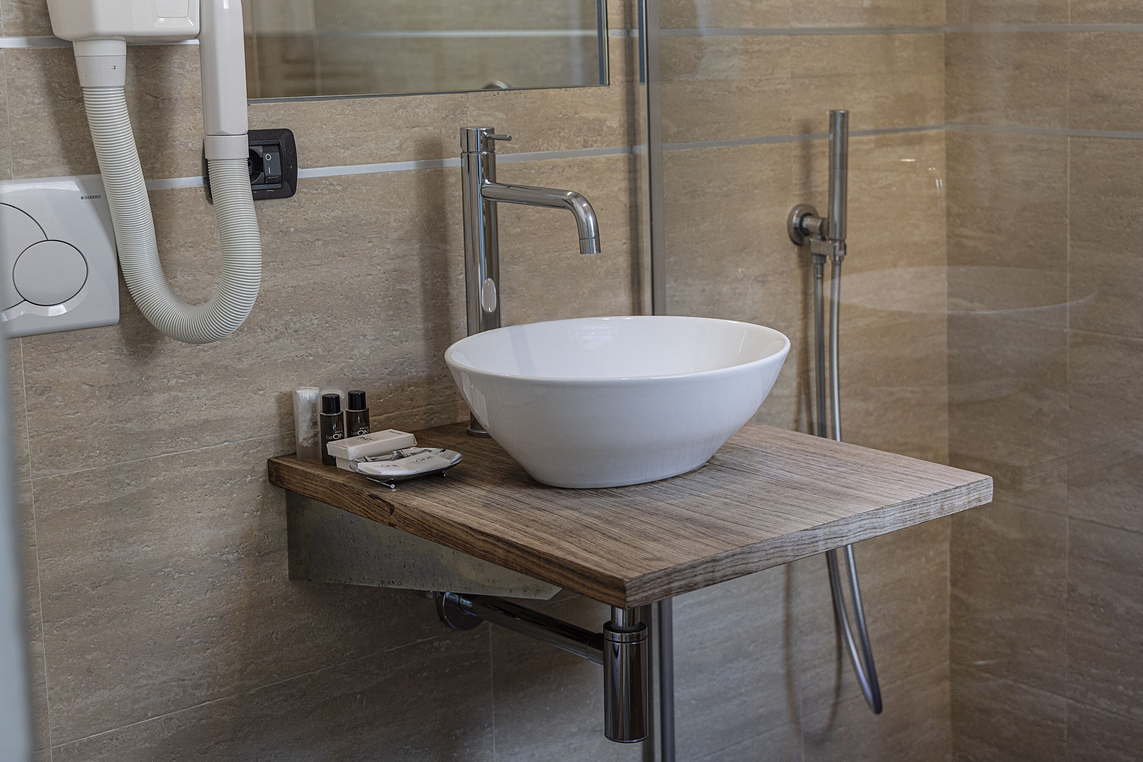 Une salle de bain avec un lavabo blanc, un plan de toilette en bois, un miroir et une douche.