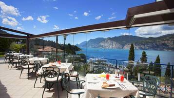 An outdoor dining area with tables and chairs, overlooking a scenic lake and mountains.