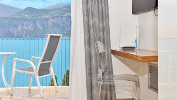Un balcon avec une chaise blanche, une chaise en plastique transparent et une table sur laquelle est posée une télévision à écran plat.