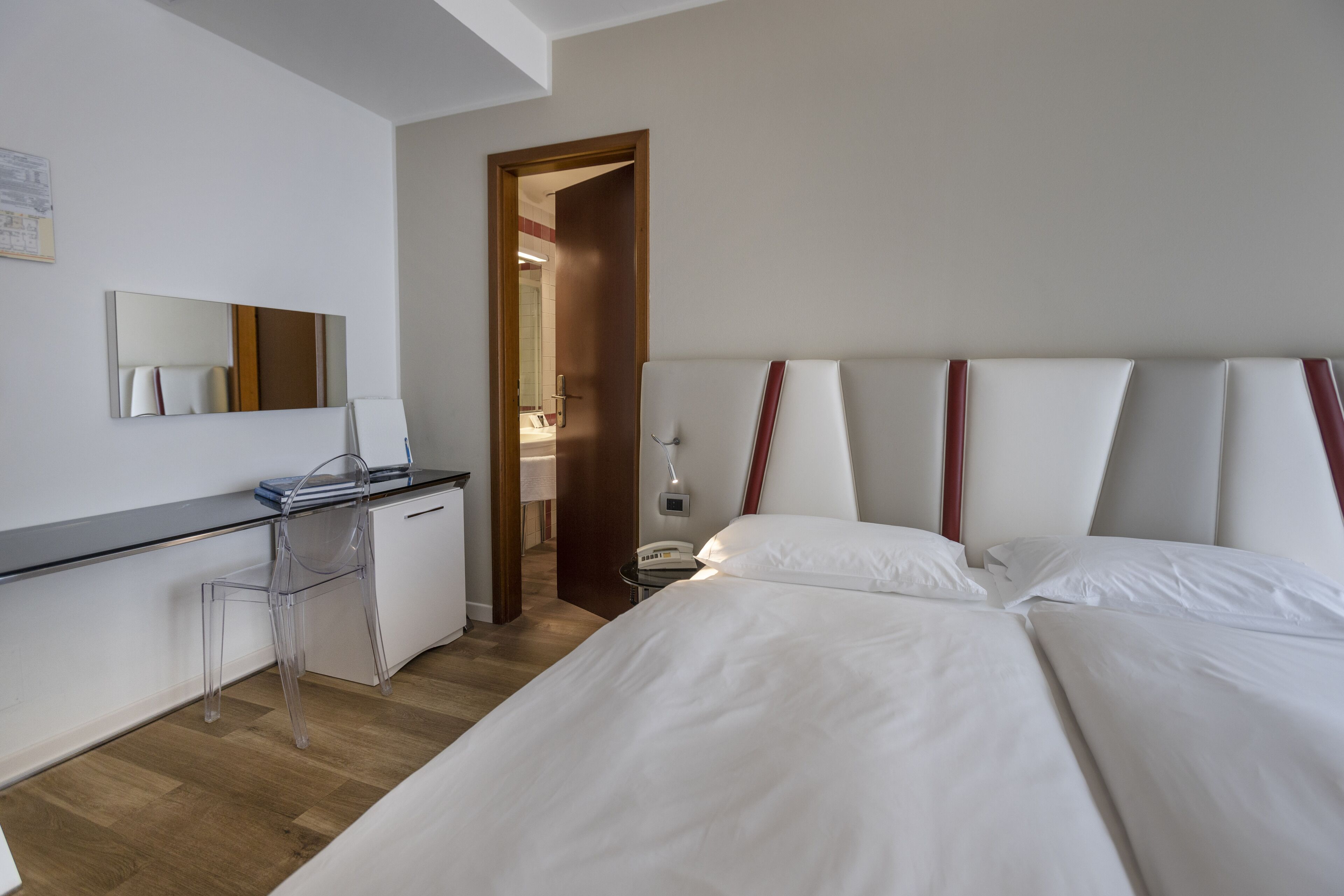 Habitación de hotel con cama, escritorio, silla, espejo y puerta que da a otra habitación.