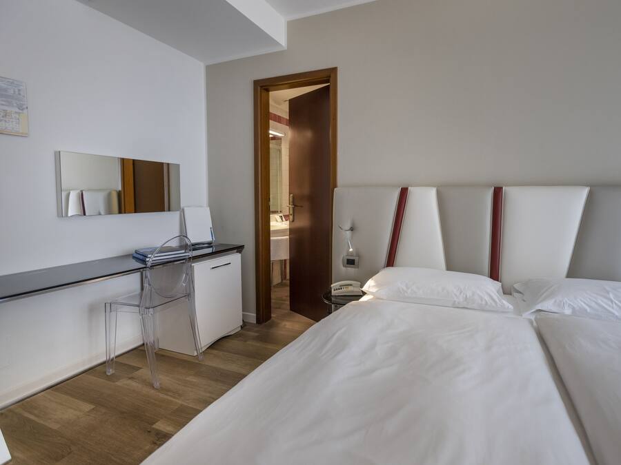 Habitación de hotel con cama, escritorio, silla, espejo y puerta que da a otra habitación.