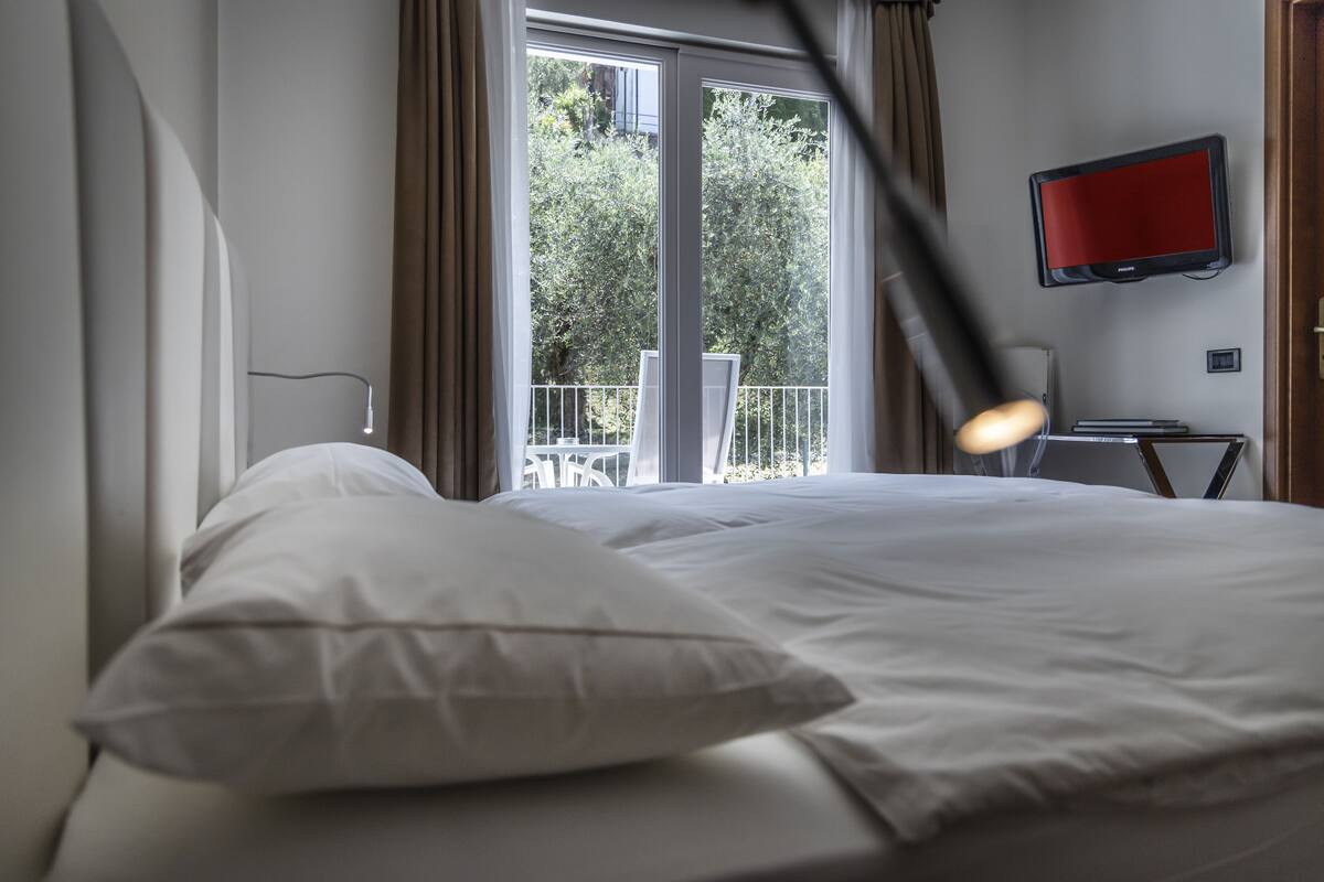 Habitación de hotel con cama, televisión montada en la pared y balcón con vistas a zonas verdes.
