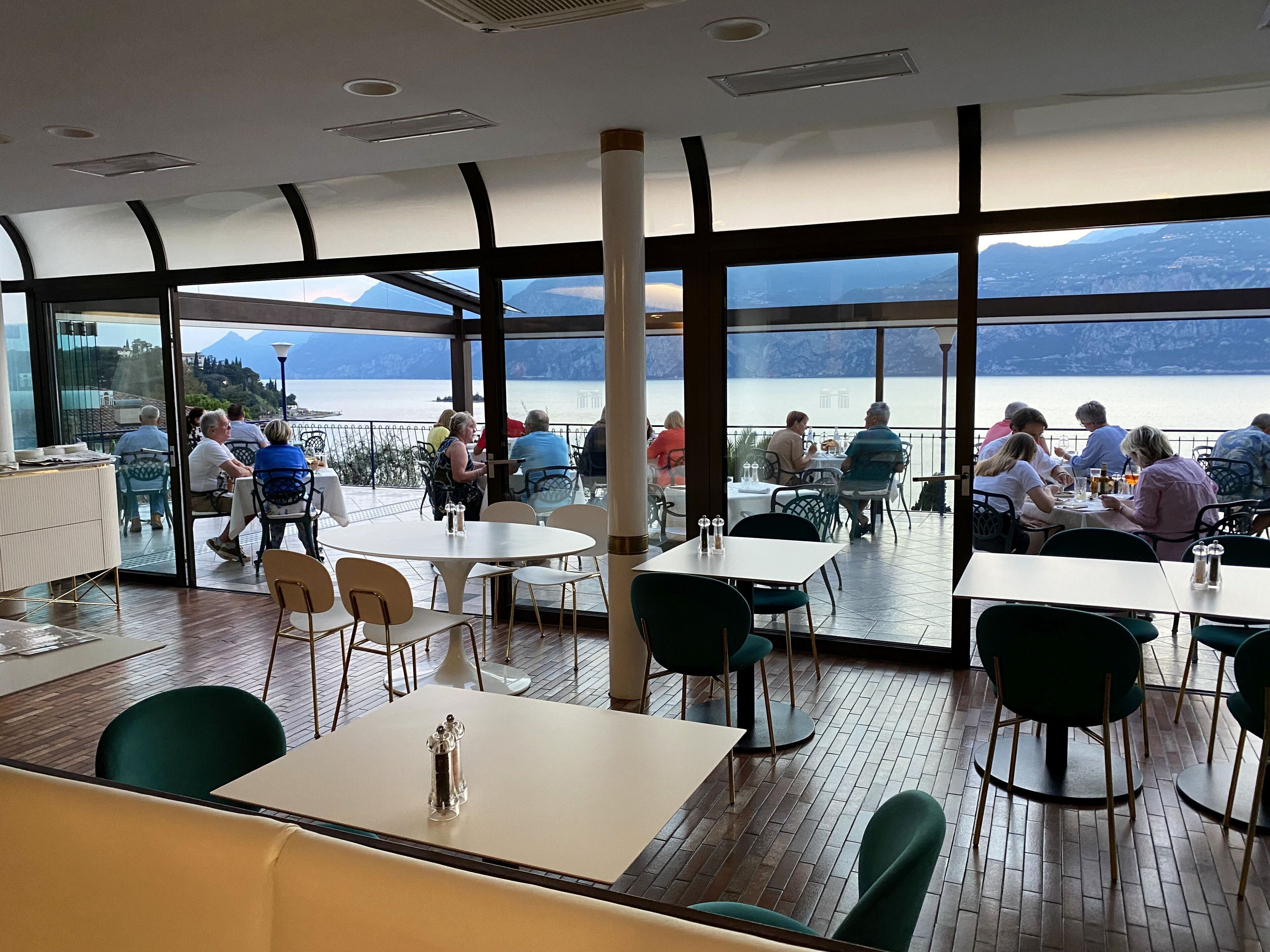 A restaurant with large windows offering a view of a lake and mountains. Tables and chairs are arranged for dining.