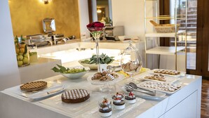 A buffet table with various desserts and a decorative vase with roses. - Hotel Capri (Malcesine)