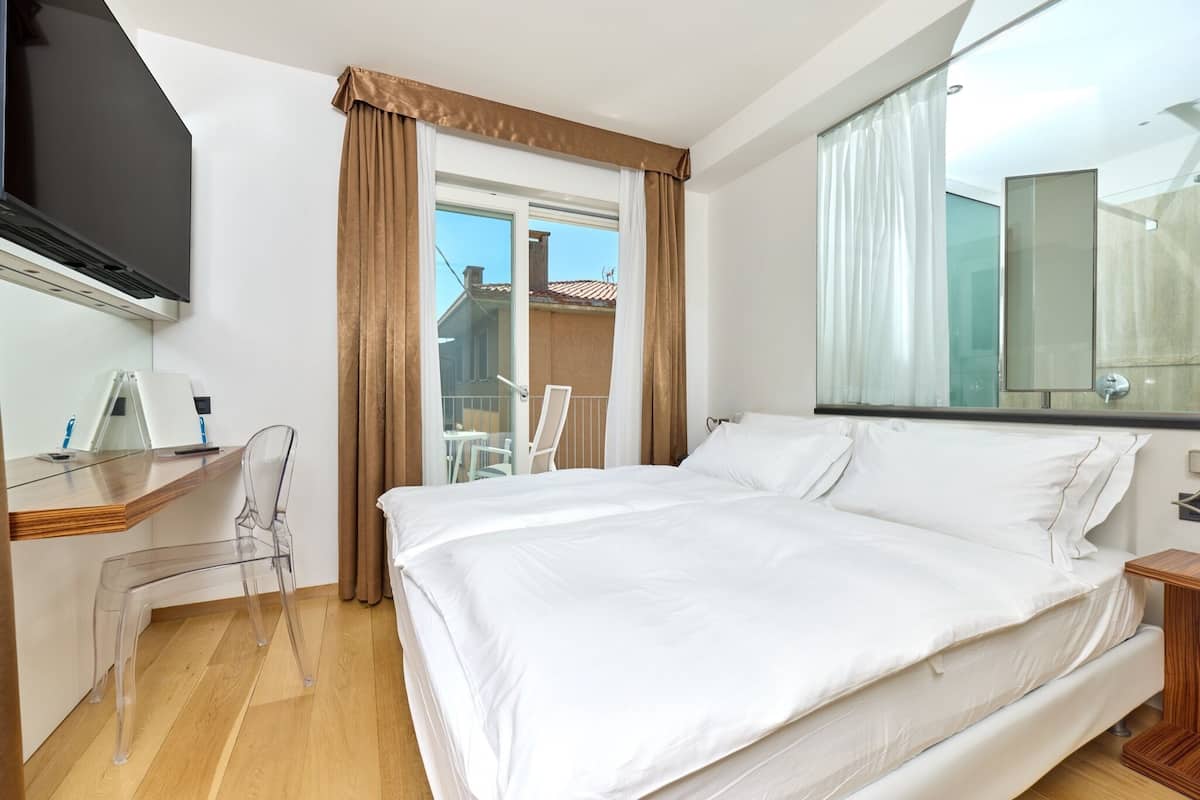 Habitación de hotel con una cama, un escritorio con silla, televisión y un amplio ventanal con cortinas.