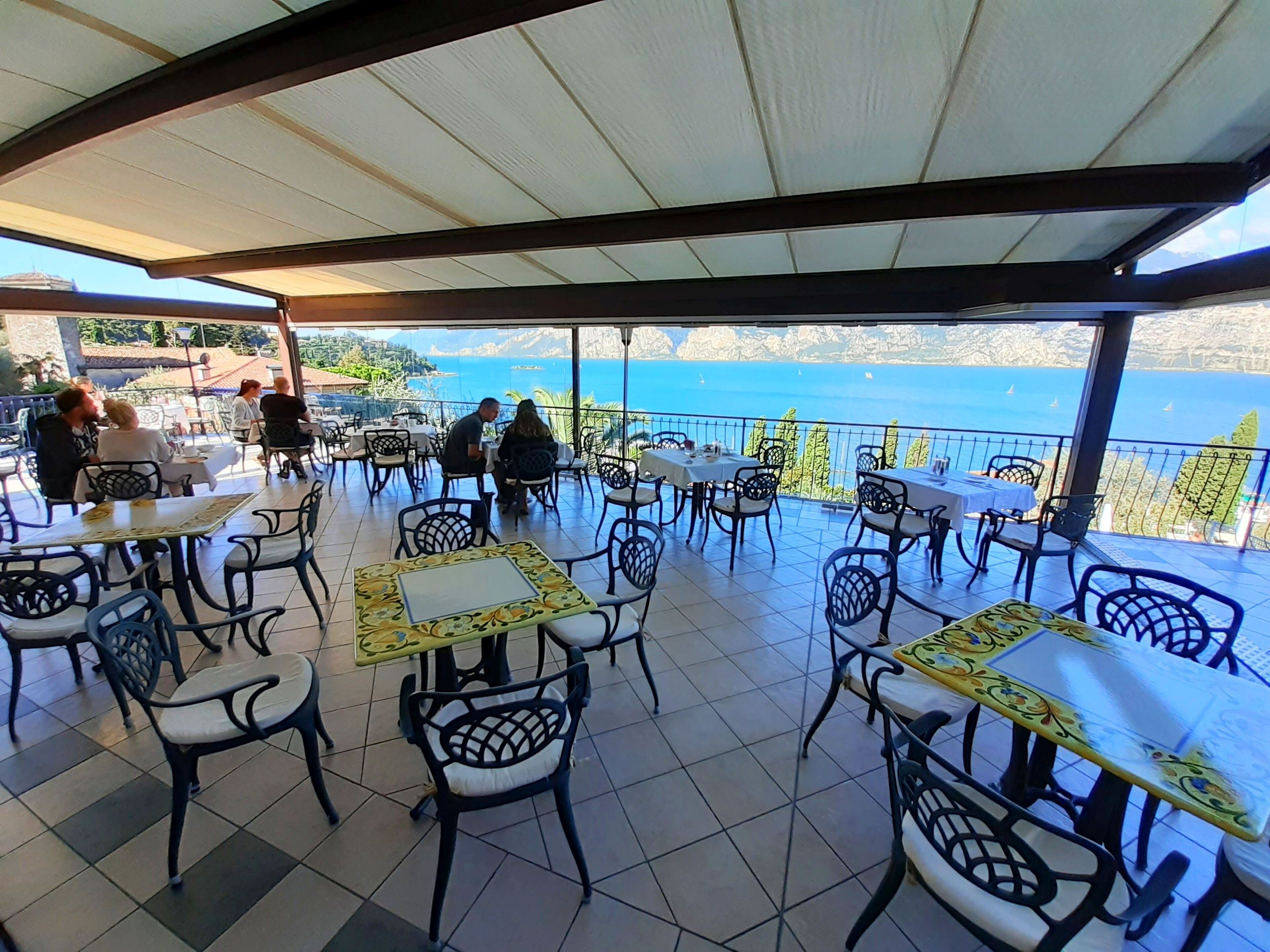 An outdoor café with tables and chairs, overlooking a scenic view of the sea and hills.