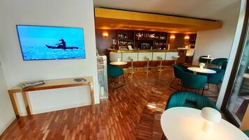 Zona bar moderna con pavimento in legno, sgabelli da bar e un televisore che mostra una scena con una barca.